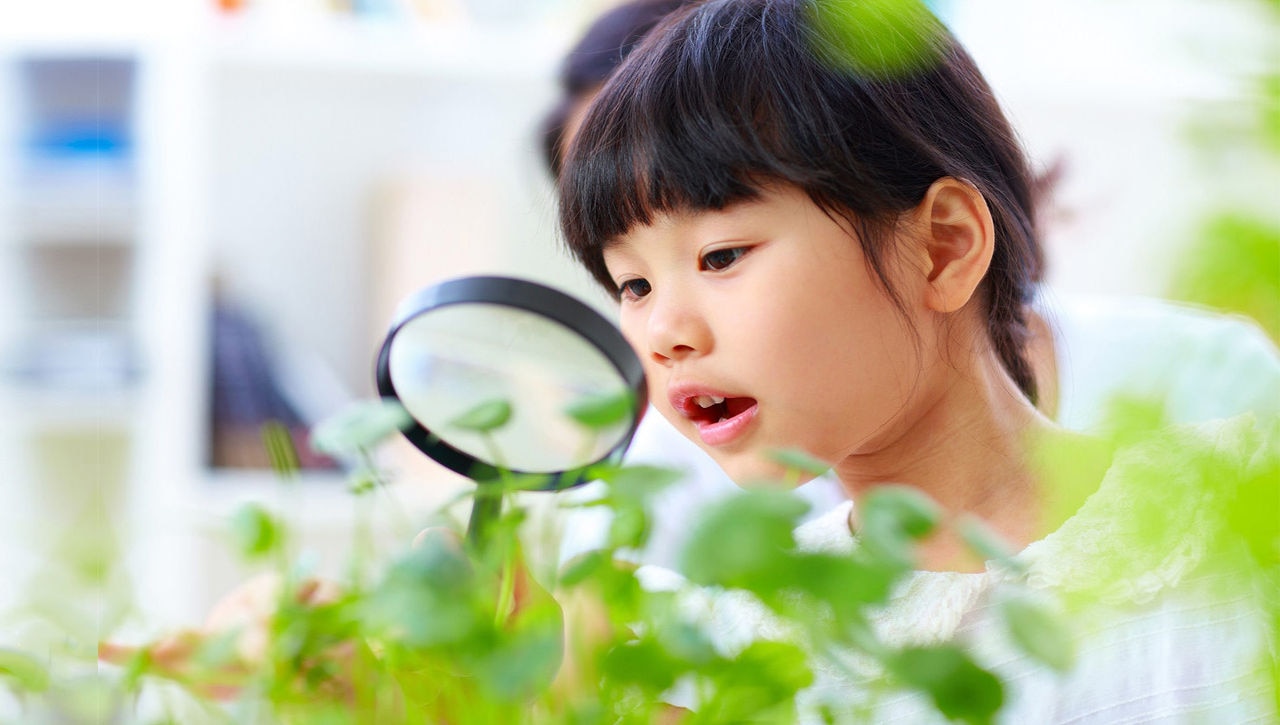 Young girl looking at plants with magnifying glass